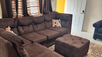 A brown sectional sofa with a matching ottoman, a patterned rug, and a door with a window in the background.