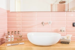 Ein Badezimmer mit einem großen weißen Waschbecken, rosa gefliesten Wänden, einem Spiegel und einer Dusche.