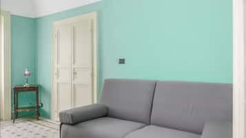 Une pièce avec un canapé gris, une petite table avec une lampe et une porte blanche.