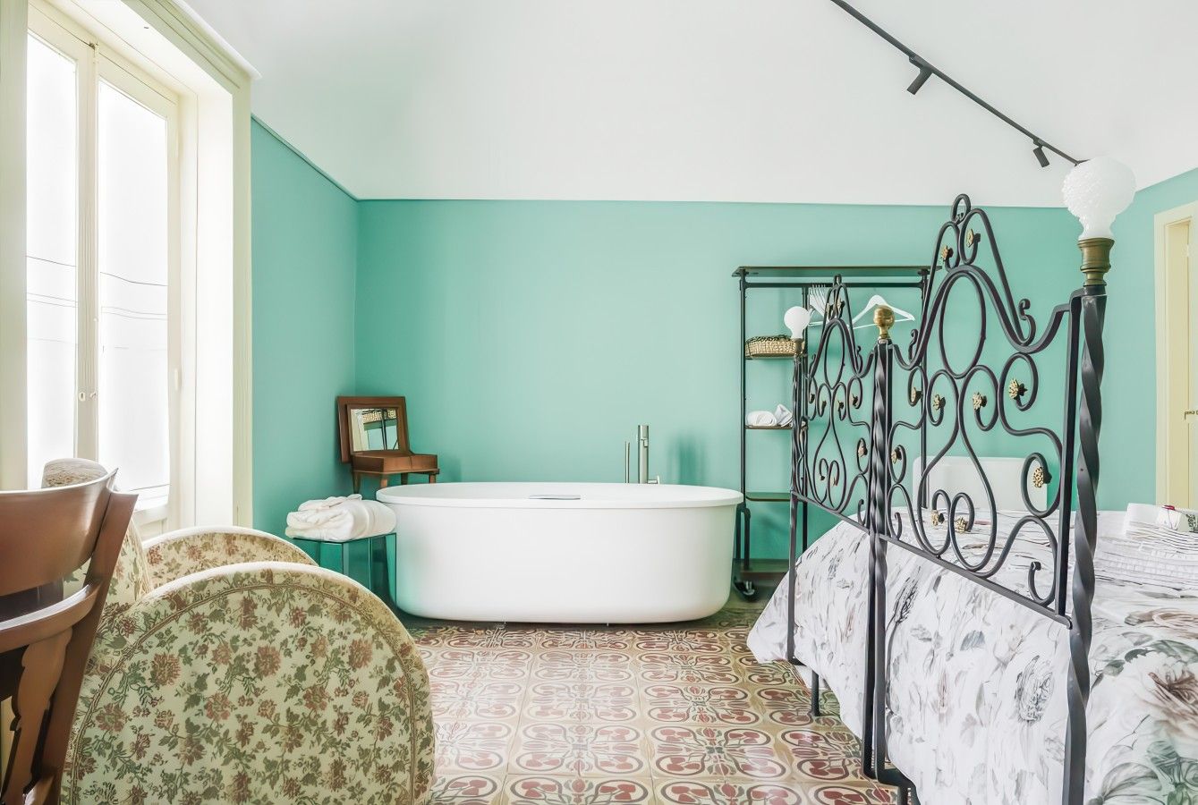 A bathroom with a freestanding bathtub, a vanity with a mirror, and a bed with a metal frame.