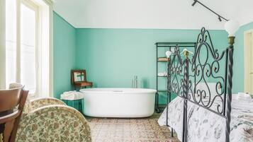 A bathroom with a freestanding bathtub, a vanity with a mirror, and a bed with a metal frame.
