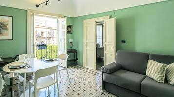 A room with a dining table, chairs, a sofa, and a patterned floor.