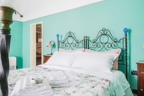 Ein Bett mit floralem Überwurf, ein Nachttisch mit Lampe und eine türkis-farbene Wand.