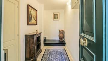 Un corridoio con una porta scura, un piccolo ripiano con oggetti decorativi, un tappeto e due quadri appesi al muro.