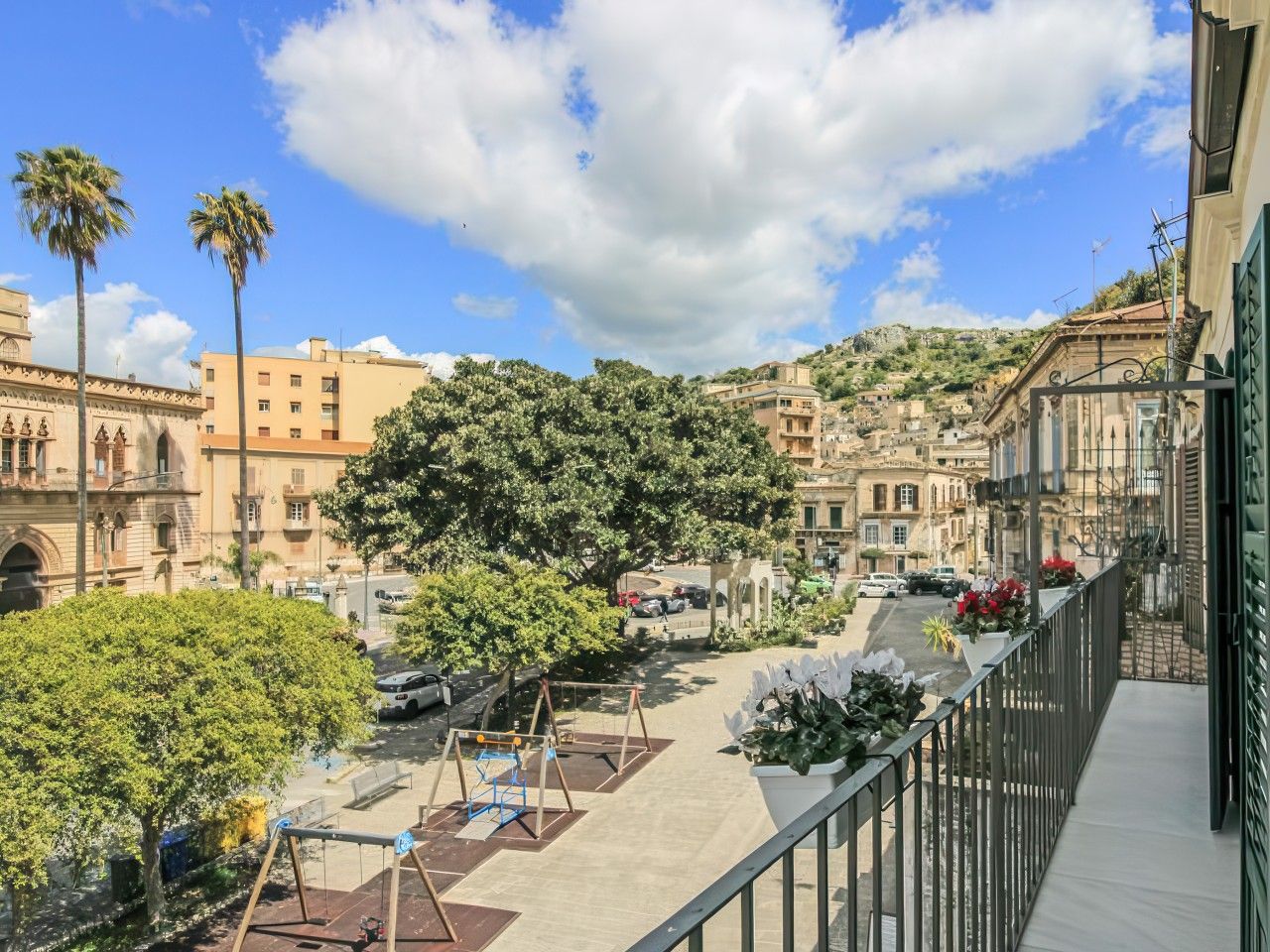 A balcony with a view of a courtyard, including a swing set and a tree.