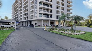 Eine mehrstöckige Parkgarage mit überdachtem Eingang, neben einem Gebäude mit Balkonen und einem begrünten Bereich mit Palmen.