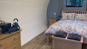 A compact, modern bedroom with a curved ceiling, a bed with floral bedding, a wooden dresser, and a small table with towels.