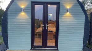 A small, single-story building with a dark wooden door and two exterior wall-mounted lights.