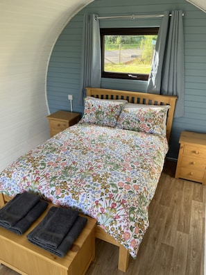 A bedroom with a wooden bed, floral bedding, a window with curtains, and a wooden nightstand.