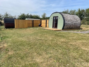 A fenced backyard with a small shed and a larger, curved structure.