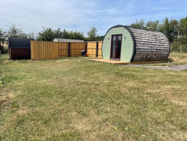 A fenced backyard with a small shed and a larger, curved structure.