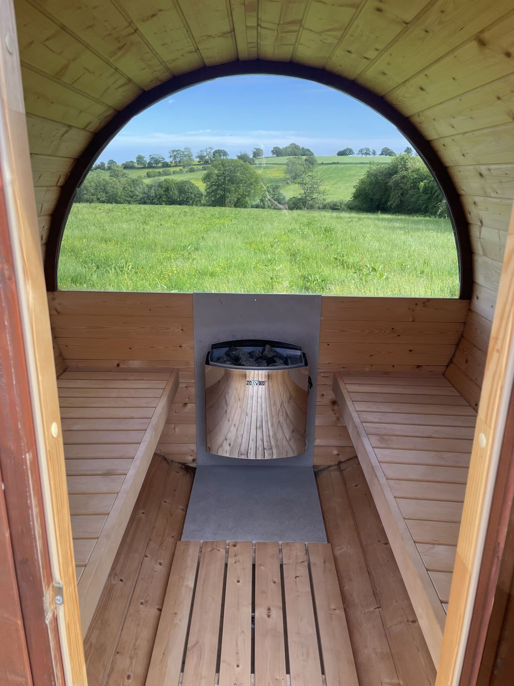A wooden sauna with a view of a green field through an arched opening.