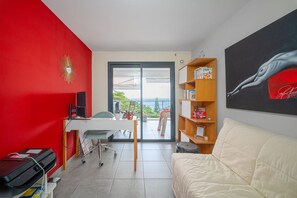 Quarto com parede vermelha, sofá branco, escrivaninha com computador, estante de livros e um quadro.