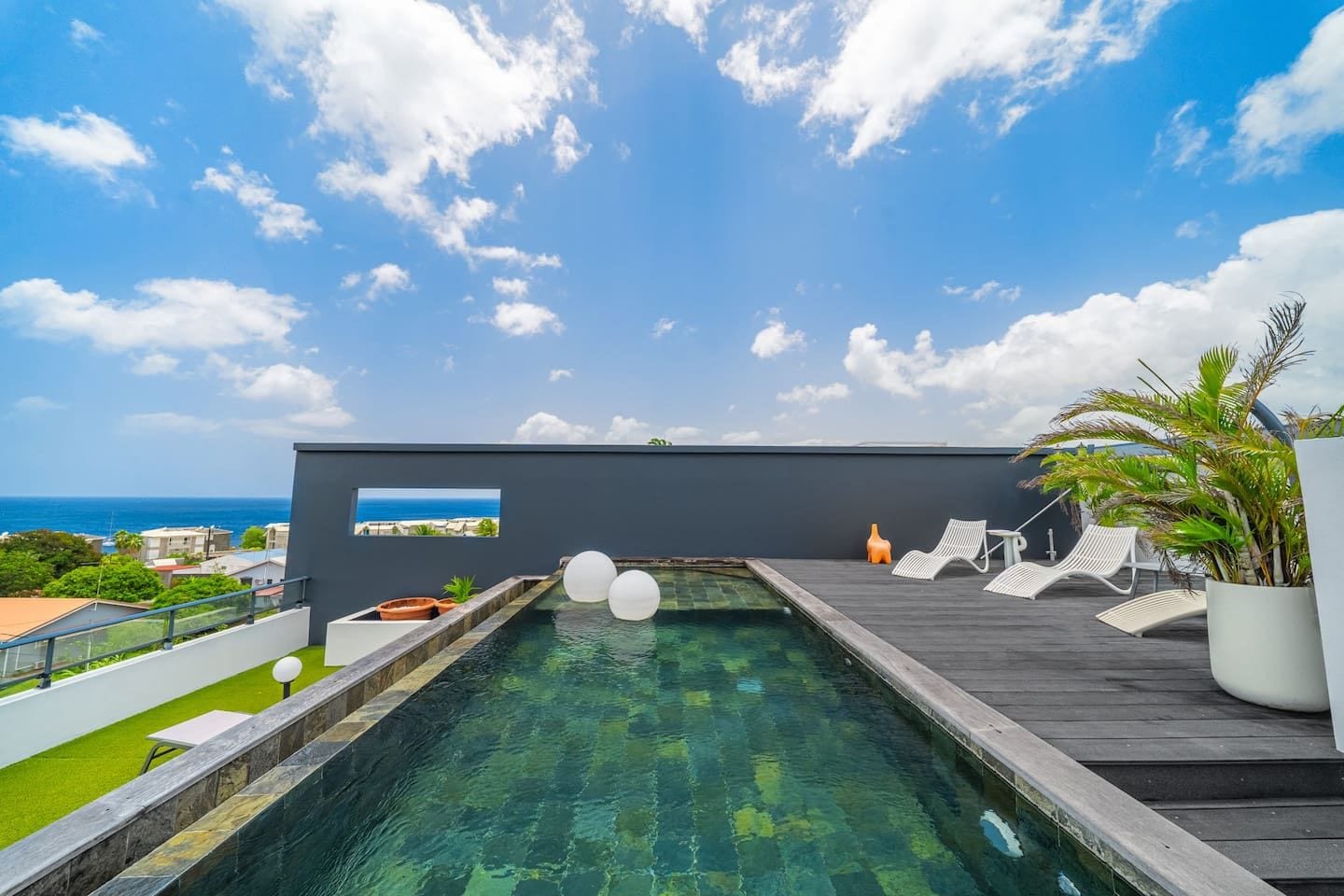 A rooftop pool with clear water, a view of the ocean, and lounge chairs.