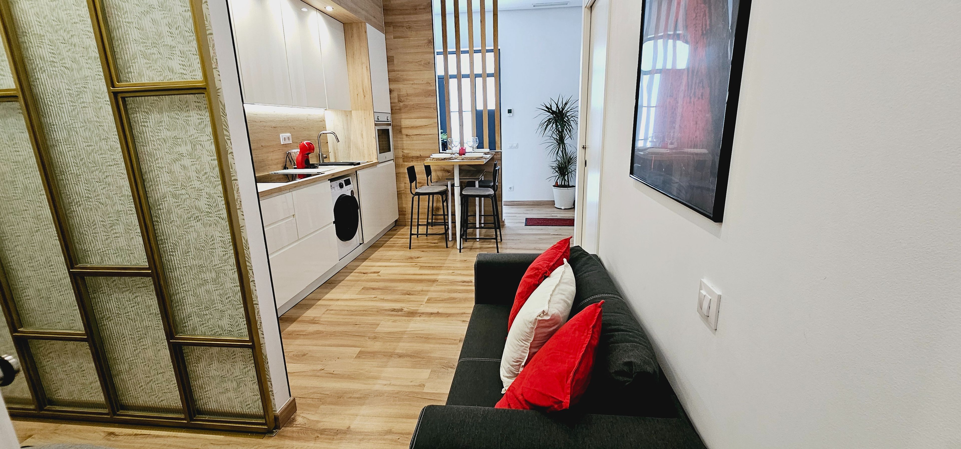 Eine moderne Küche mit Geschirrspüler, ein Essbereich mit Tisch und Stühlen sowie ein Wohnbereich mit Sofa und Kissen.