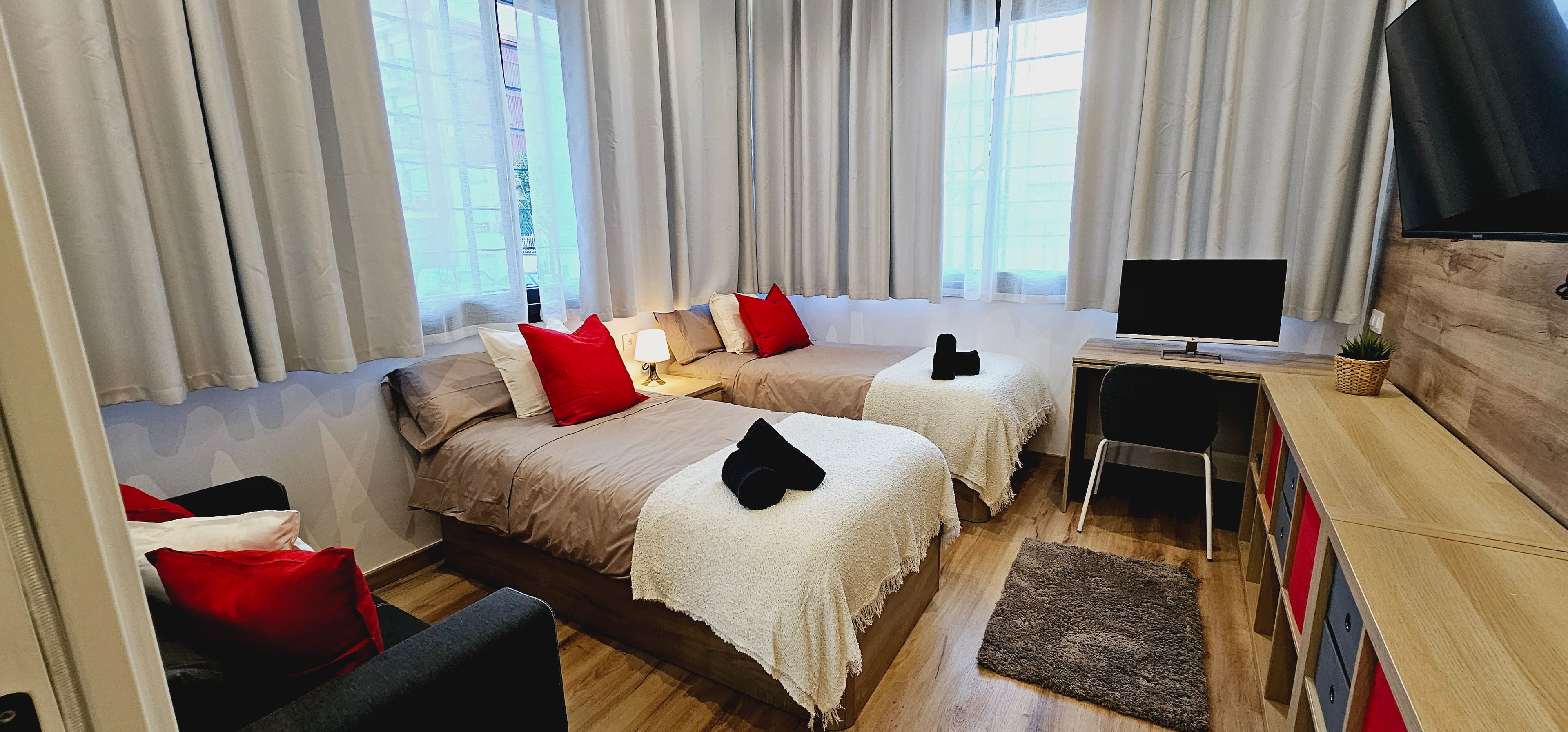 Ein Hotelzimmer mit zwei Betten, einem Fernseher, einem Schreibtisch und einem Sessel.