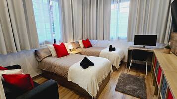 Ein Hotelzimmer mit zwei Betten, einem Fernseher, einem Schreibtisch und einem Sessel.