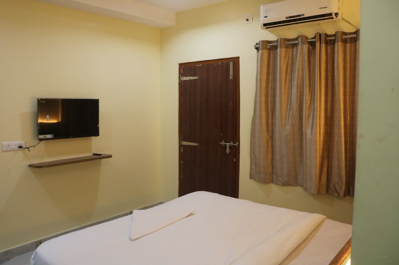 Una habitación con cama, televisión montada en la pared, una puerta y un aire acondicionado.