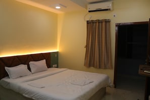 Une chambre d’hôtel avec un lit, une tête de lit, un appareil de climatisation, un rideau et une porte.