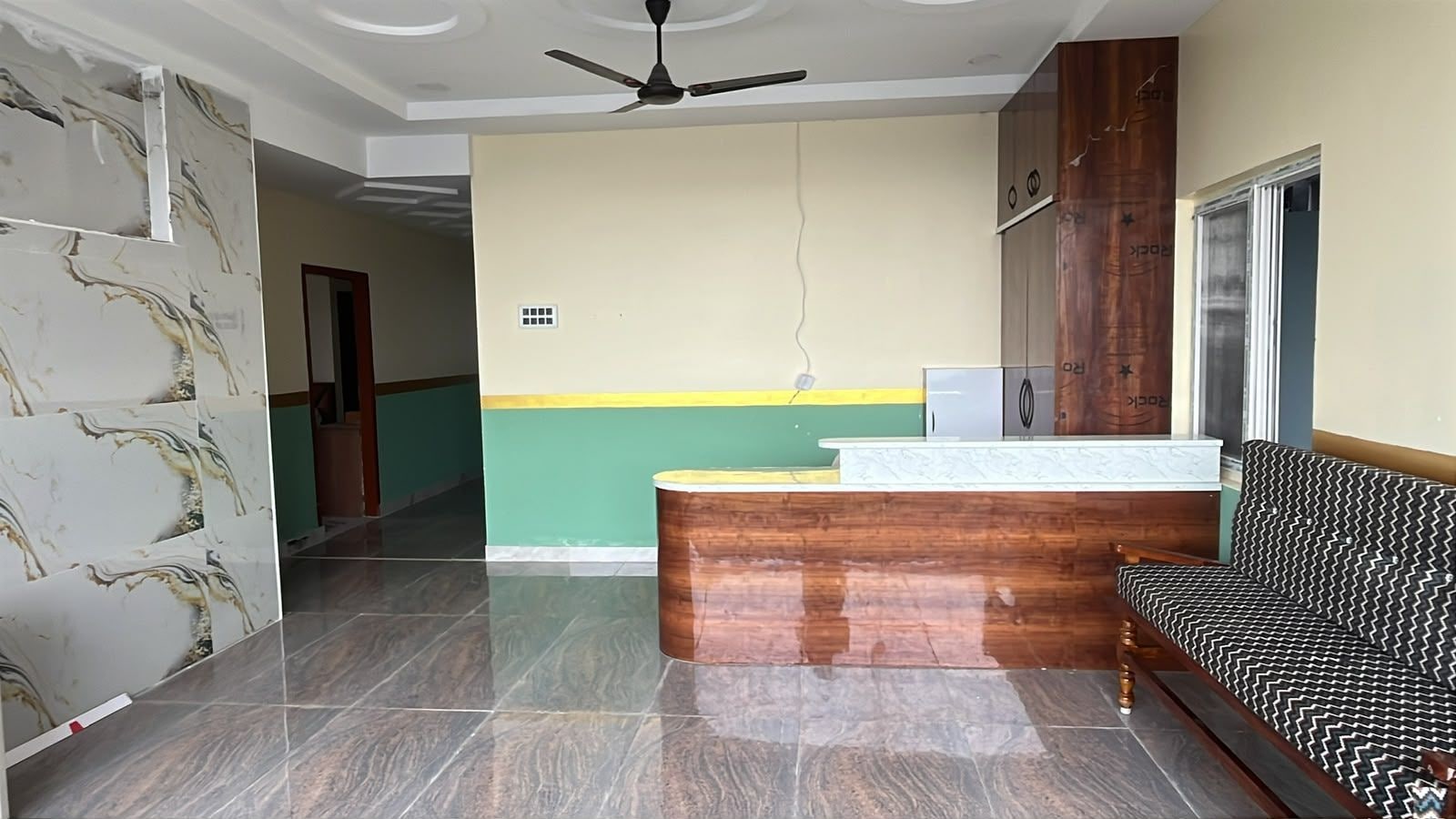 Un área de recepción con mostrador de madera, un sofá estampado y un ventilador de techo.