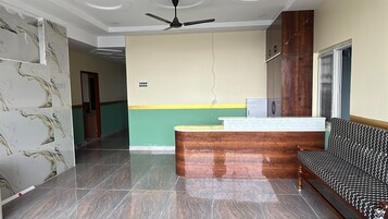 Un área de recepción con mostrador de madera, un sofá estampado y un ventilador de techo.