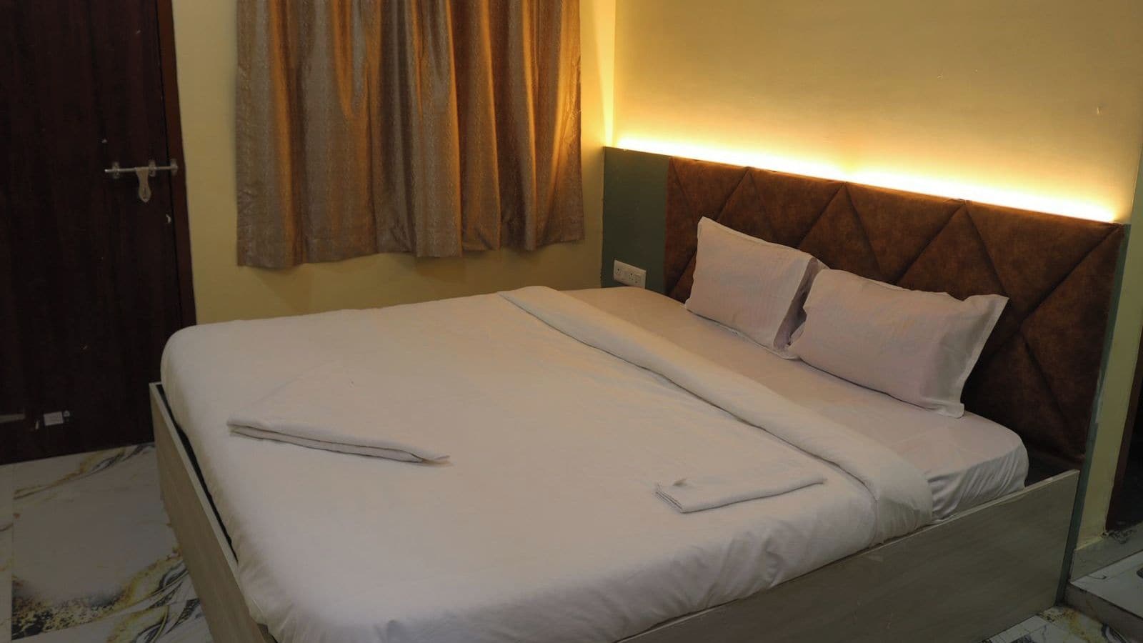 Una cama bien hecha con cabecera, mesita de noche y lámpara de pared.