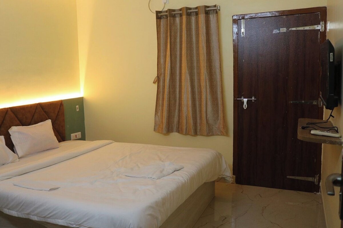 Une chambre d’hôtel avec un lit, une tête de lit en bois, un rideau, une porte et un téléviseur.