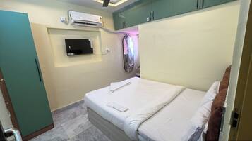 A bedroom with a bed, an air conditioning unit, a television, and a wardrobe.