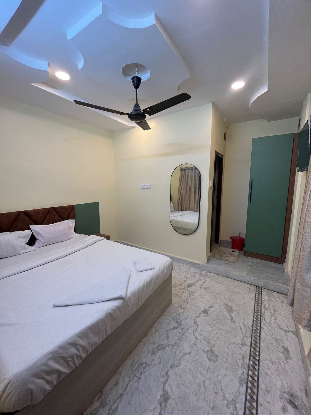 A hotel room with a bed, ceiling fan, mirror, and a small bathroom area.