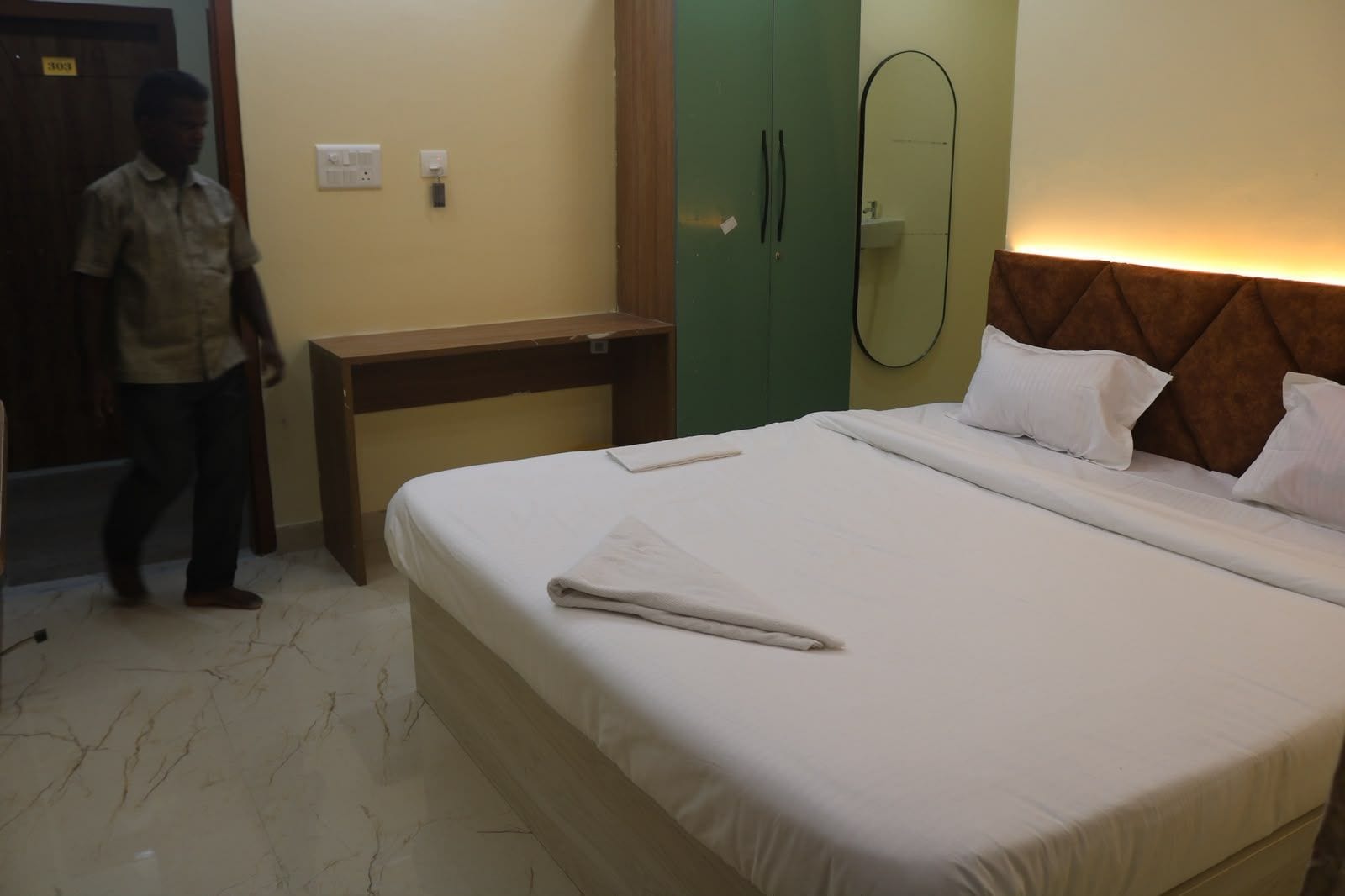 A hotel room with a bed, a bedside table, a mirror, and a wardrobe.