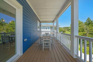 A covered porch with a table and chairs, a railing, and a view of a house and trees. - Corolla Cottage: Semi-Soundfront | Pet Friendly (Corolla)