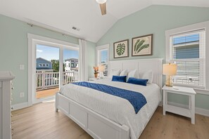 Quarto com cama grande, mesa de cabeceira, janela com persianas e vista para o exterior.