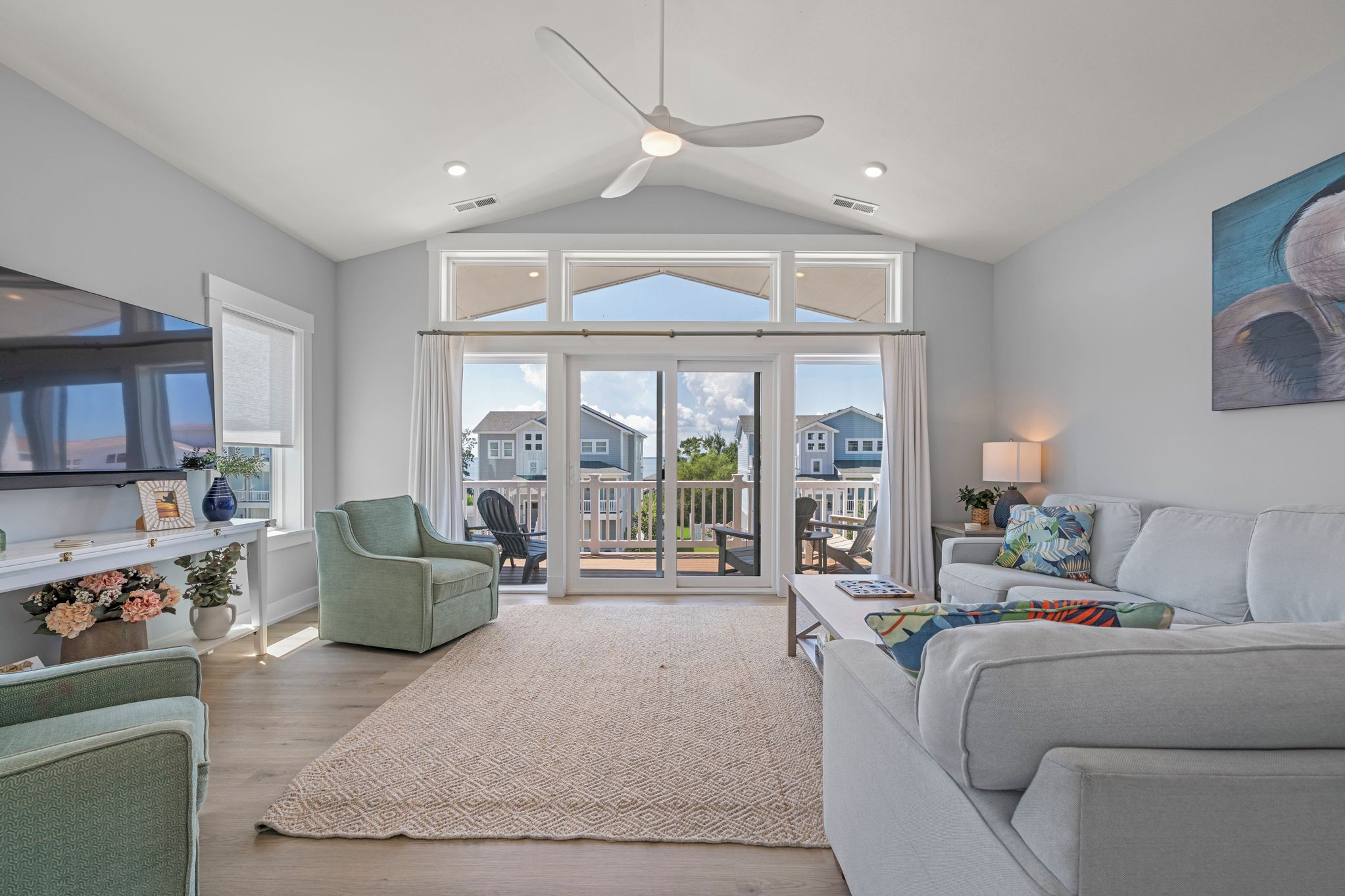 A spacious living room with a large sliding glass door leading to an outdoor patio, a ceiling fan, and a flat-screen TV mounted on the wall.