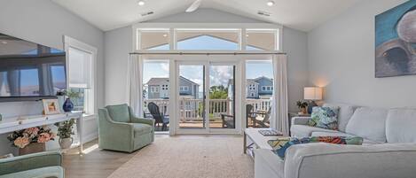 A spacious living room with a large sliding glass door leading to an outdoor patio, a ceiling fan, and a flat-screen TV mounted on the wall.