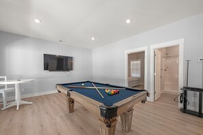 Uma mesa de bilhar com bolas, uma televisão presa na parede e uma porta que dá para uma área de chuveiro.