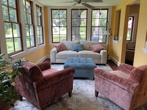 A room with a beige sofa, two armchairs, a blue ottoman, and a large window with multiple panes.
