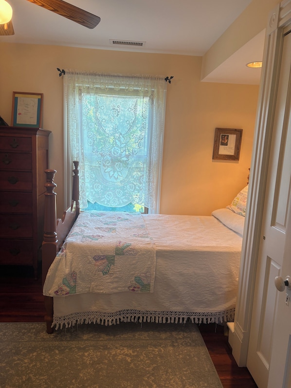 A bedroom with a bed, a dresser, a window with lace curtains, and a door.