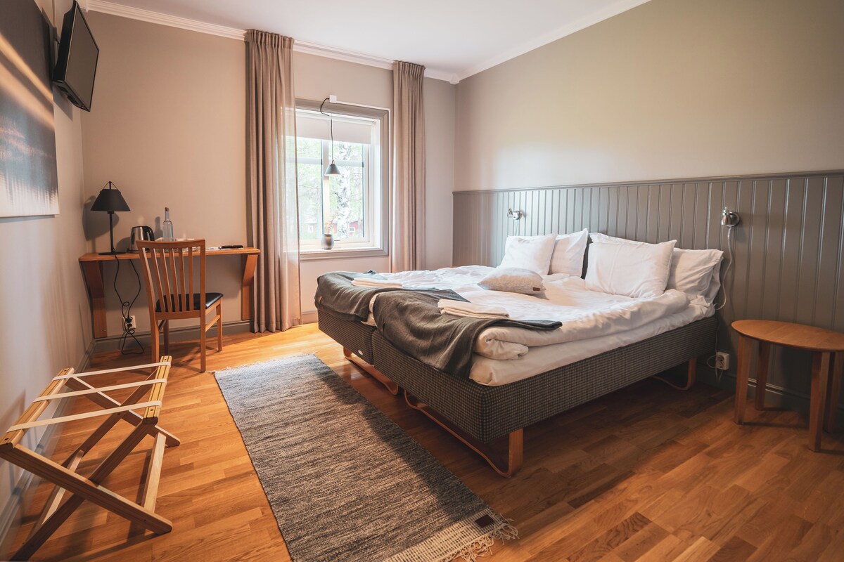 A bedroom with a bed, a desk, a chair, a lamp, and a window with curtains.