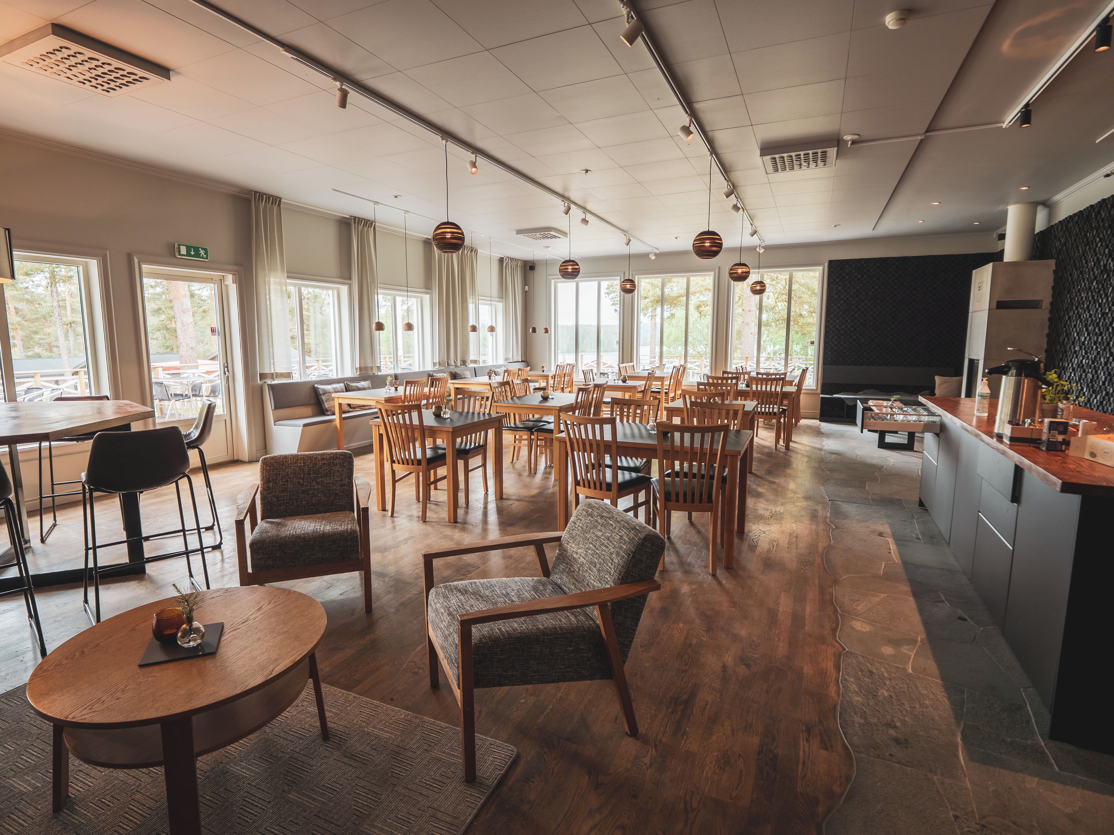 A spacious dining area with multiple tables and chairs, large windows, and a modern kitchen area.