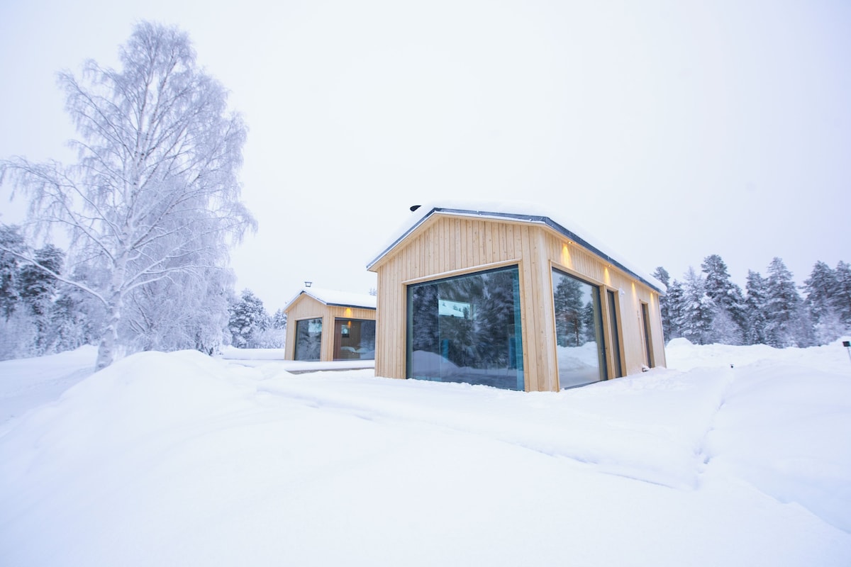 A wooden cabin with large windows, surrounded by snow-covered trees.