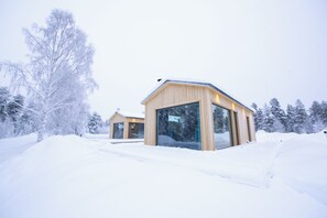 A wooden cabin with large windows, surrounded by snow-covered trees. - Sörbyn Lodge (Norrbottens län)
