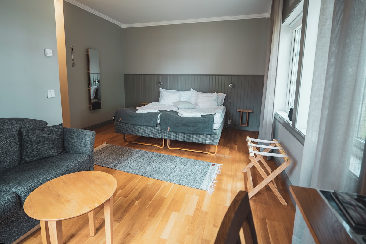 A modern bedroom with a bed, a sofa, a small table, and a window.