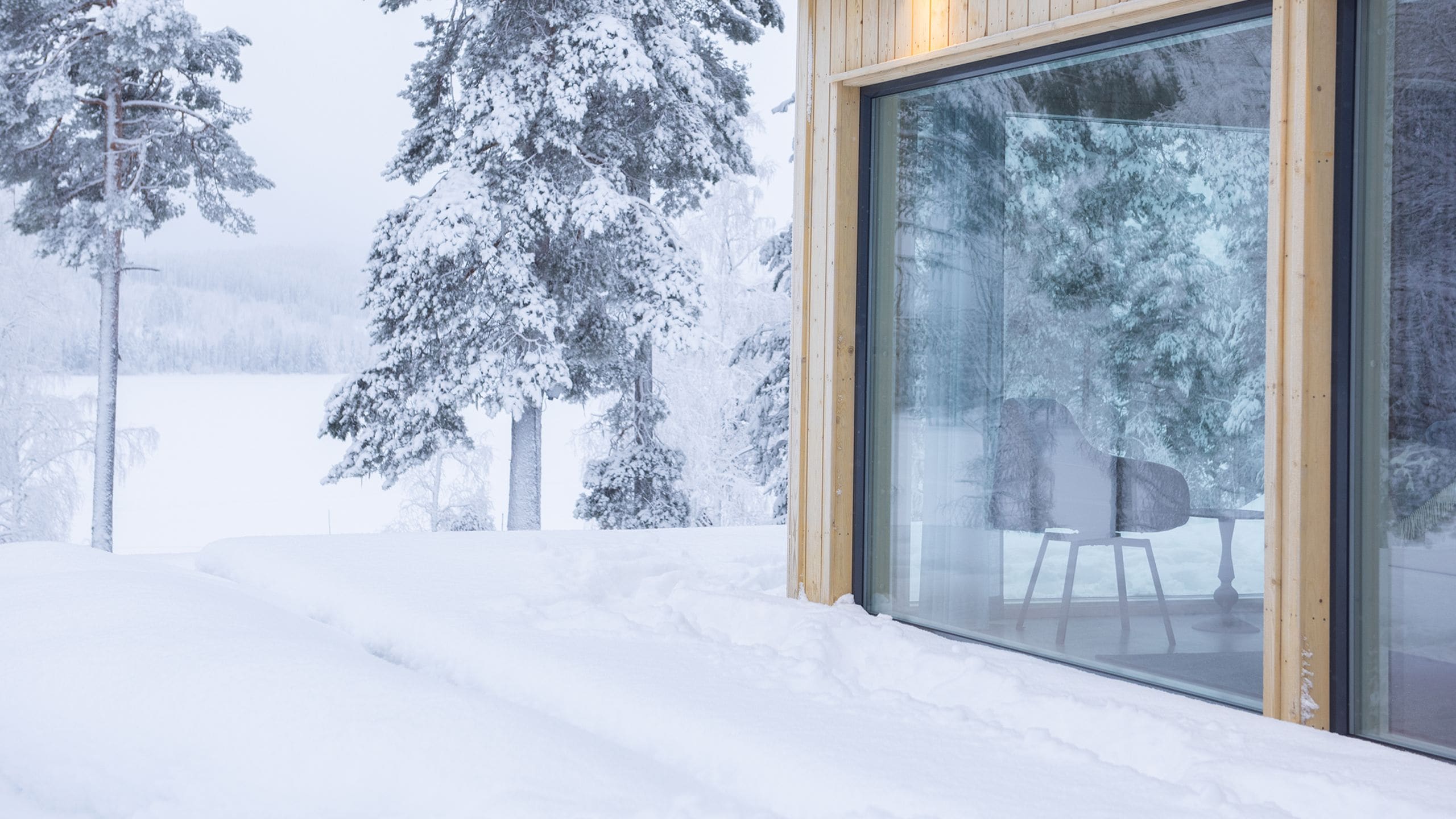 Ett snötäckt landskap med en träbyggnad som har ett stort fönster av glas.