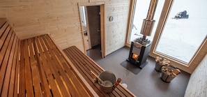 A wooden interior with a fireplace, a bench, and a view of the outside. - Sörbyn Lodge (Gunnarsbyn)