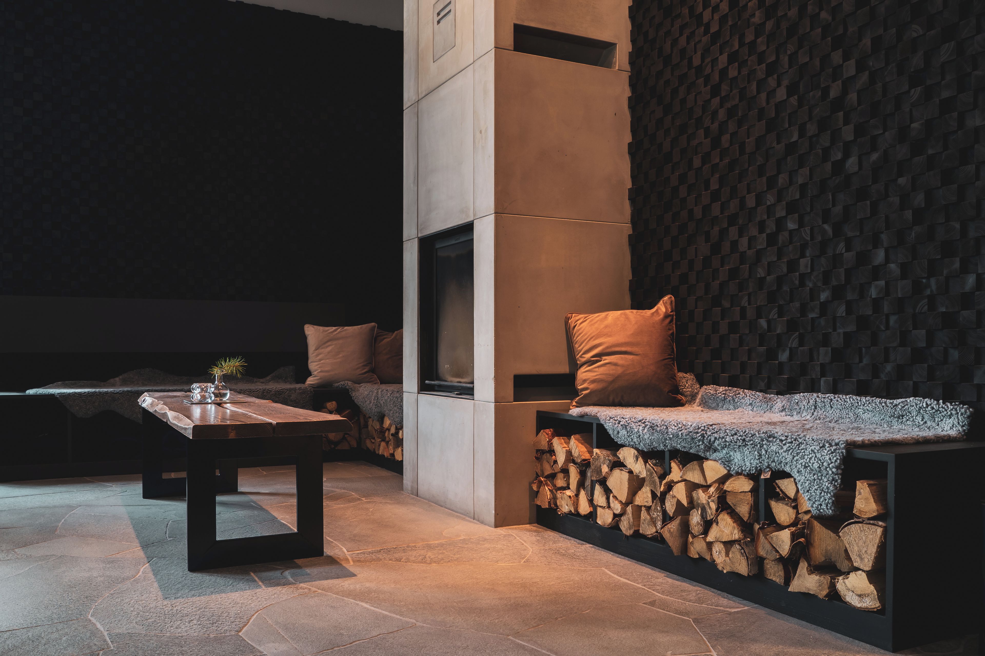 A modern interior with a stone fireplace, a seating area with cushions, and a stone wall.