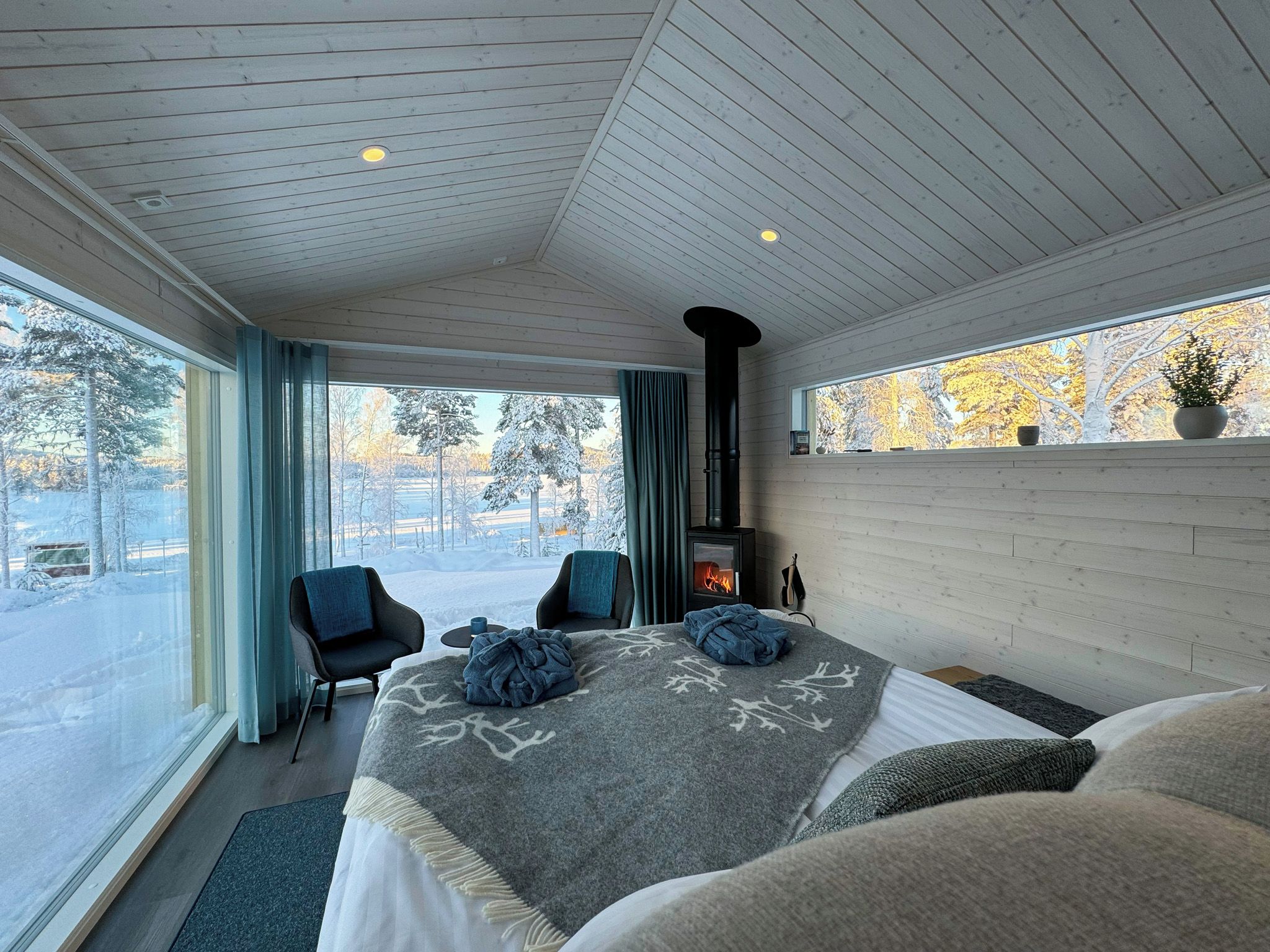 Ett modernt sovrum med en stor säng, en öppen spis och utsikt över ett snötäckt landskap.