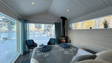 Ett modernt sovrum med en stor säng, en öppen spis och utsikt över ett snötäckt landskap.