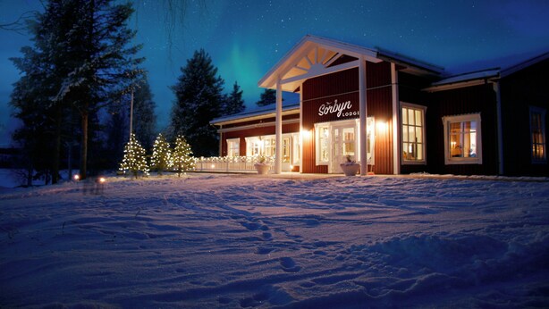 A lodge with a covered entrance, snow-covered ground, and a night sky with visible stars. - Sörbyn Lodge (Norrbottens län)