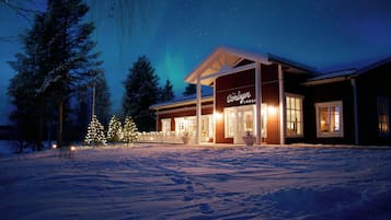 En stuga med en ingång som är skyddad av ett tak, snötäckt mark och en natthimmel med synliga stjärnor.