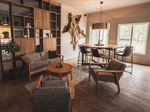 A modern living room with a wooden sofa, a round coffee table, and a dining area with chairs and a table.